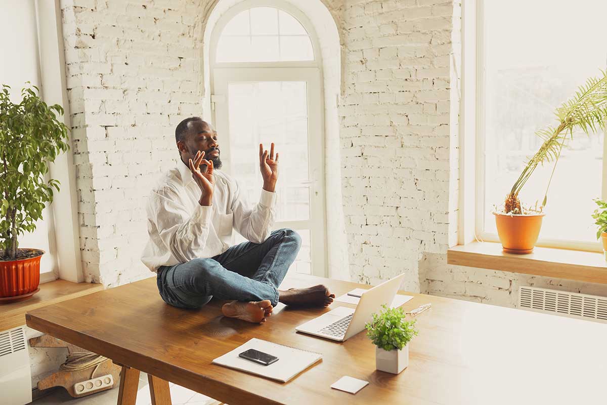 Young african-american man doing yoga at home while being quarantine and freelance working